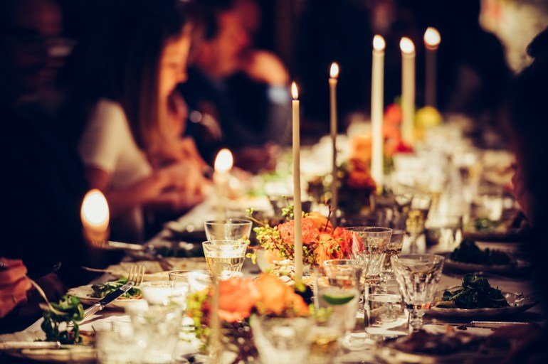 People enjoy a family dinner with candles. Big table served with food and beverages.
